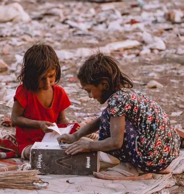 two little girls are looking at the picture in the book which they have found from garbage.